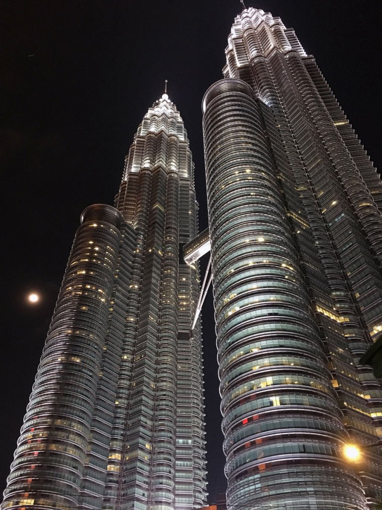 lit up metal skyscrapers against a black night sky shot from below looking upwards