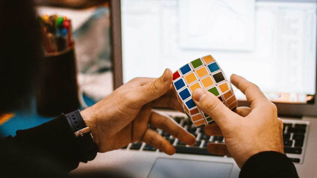 Hands holding a rubik's cube in front of a laptop screen.