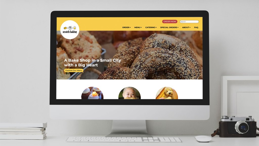 Desktop computer screen  on a white desk with a webpage for Scratch Baking featuring a photo with bagels
