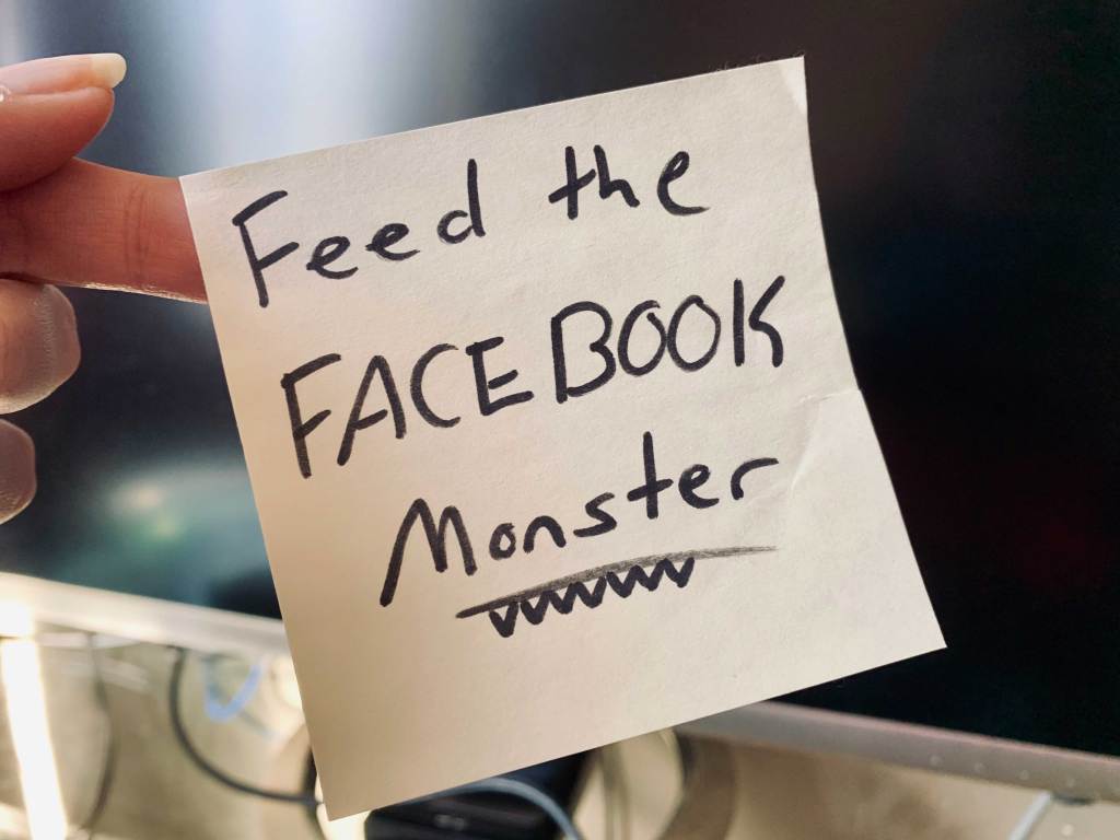 Post-it note being held by hand that says "Feed the Facebook Monster"