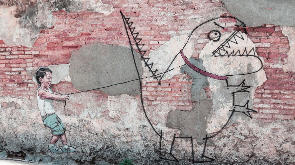 Graffiti on a brick wall depicting a little boy holding the leash of a monster which looks like it was hand drawn by a child.