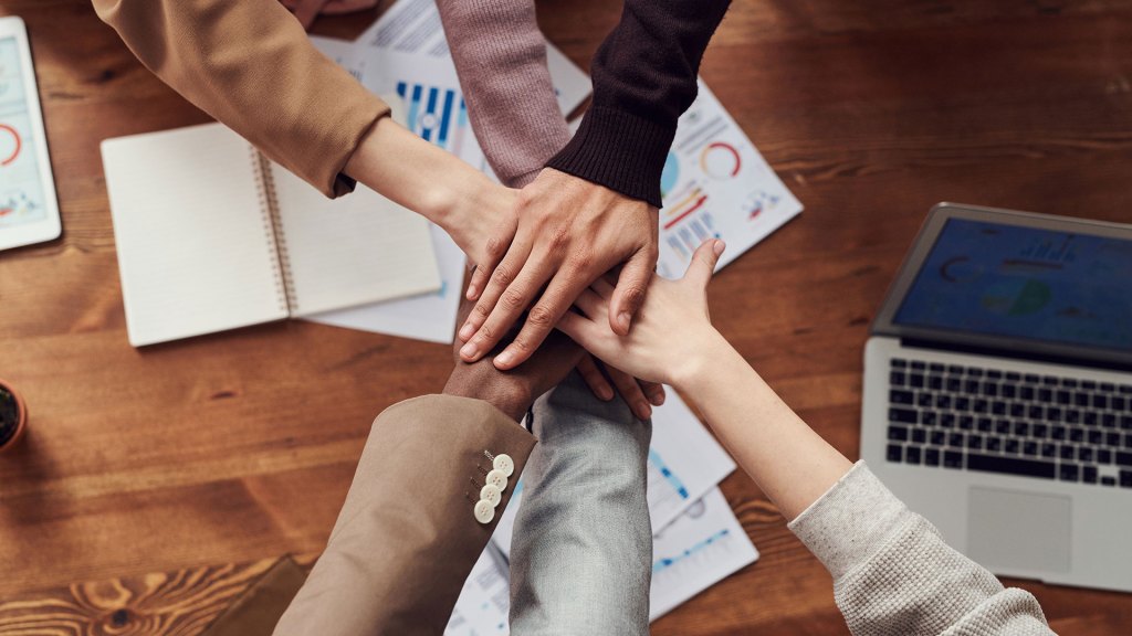 6 people's hands together over a table with business papers on it